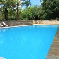 Una piscina azul cristalina con sillas de descanso y un muro de piedra.