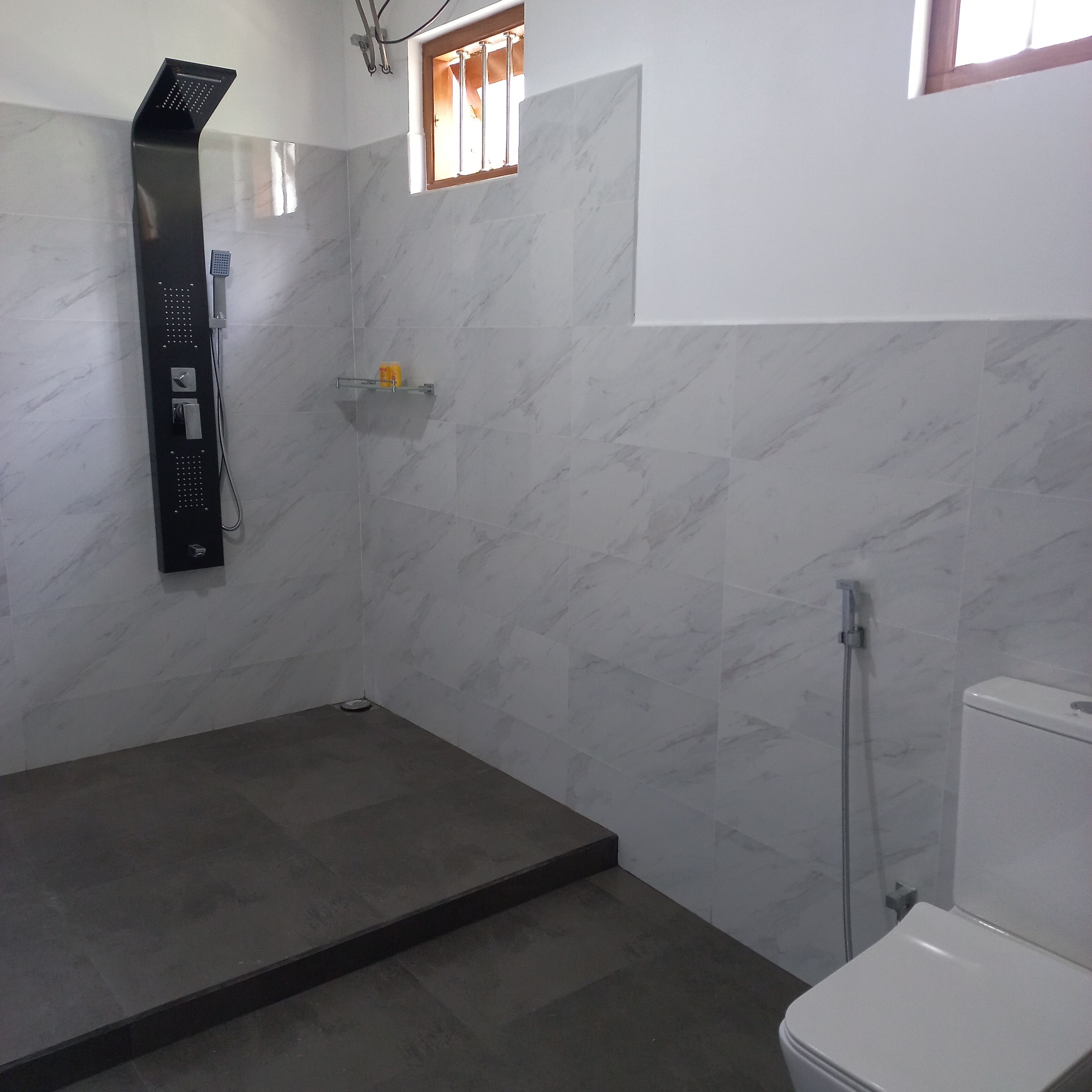 Ein Badezimmer mit Dusche, Toilette und einem kleinen Fenster.