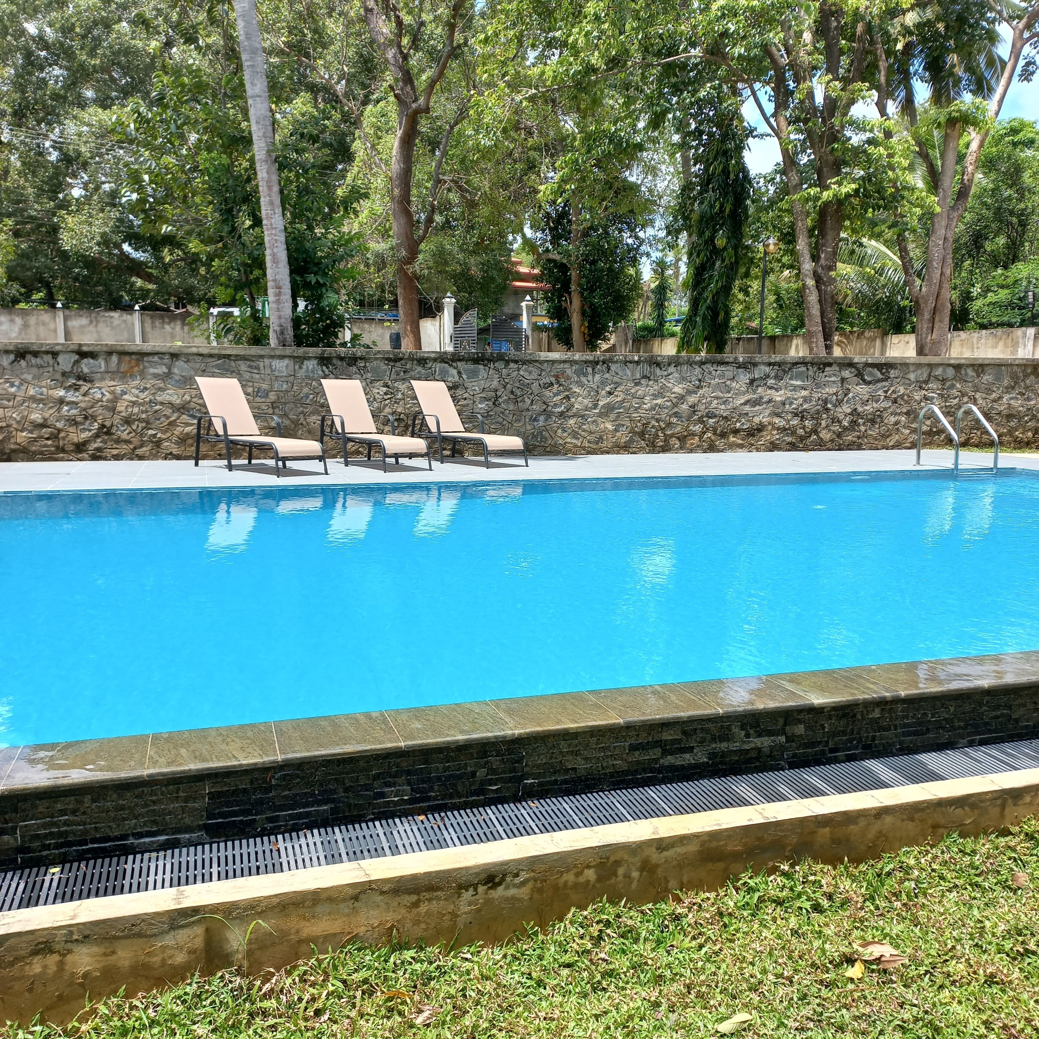 A swimming pool with three lounge chairs and a stone wall.