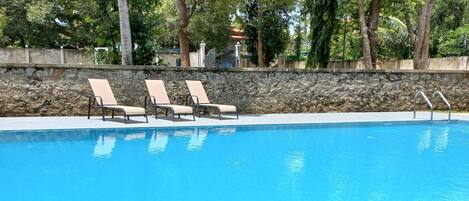 A swimming pool with three lounge chairs and a stone wall.