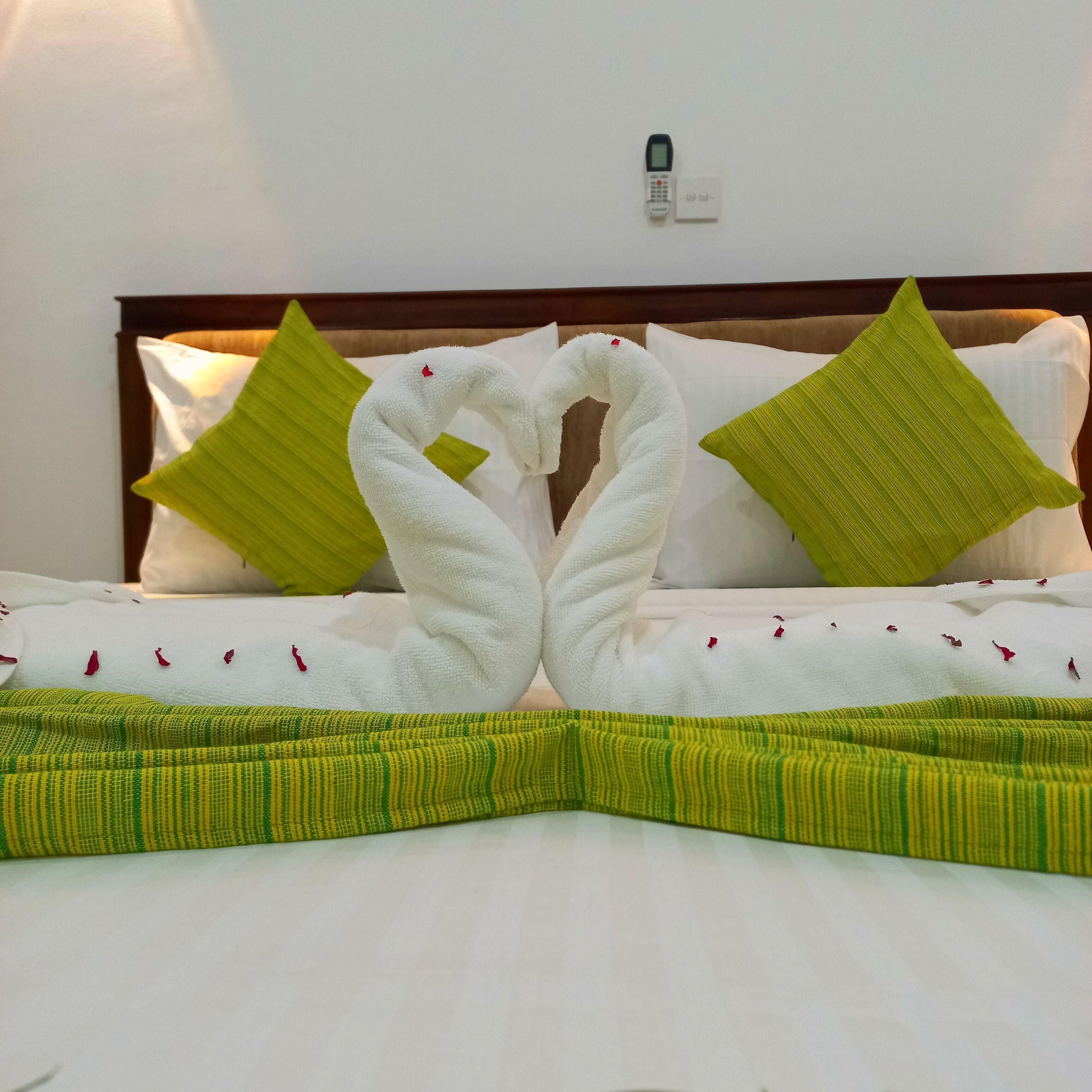 A neatly made bed with a towel arranged in a swan shape, green pillows, and a striped green and yellow bedspread.