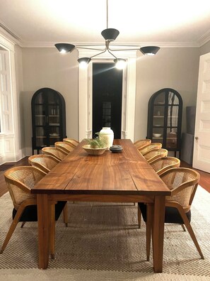 A dining room with a long wooden table, wicker chairs, a central vase, and a chandelier.