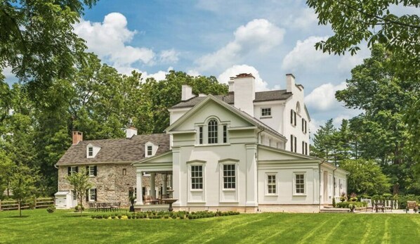 A large, two-story house with a stone facade and a white exterior, surrounded by lush greenery and a well-maintained lawn.