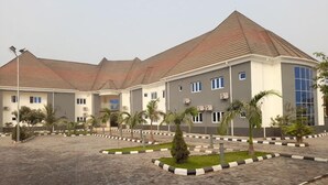 A multi-story building with a tiled roof, surrounded by a paved courtyard with palm trees and a landscaped garden.