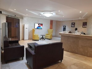 A reception area with a counter, two yellow armchairs, a dark brown sofa, a television, and a refrigerator.