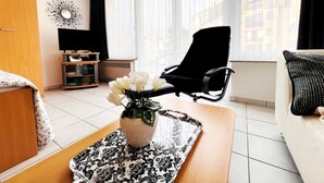 Ein Hotelzimmer mit einem Bett, einem Fernseher, einem schwarzen Bürostuhl, einem weißen Sofa und einem Fenster mit Vorhängen.