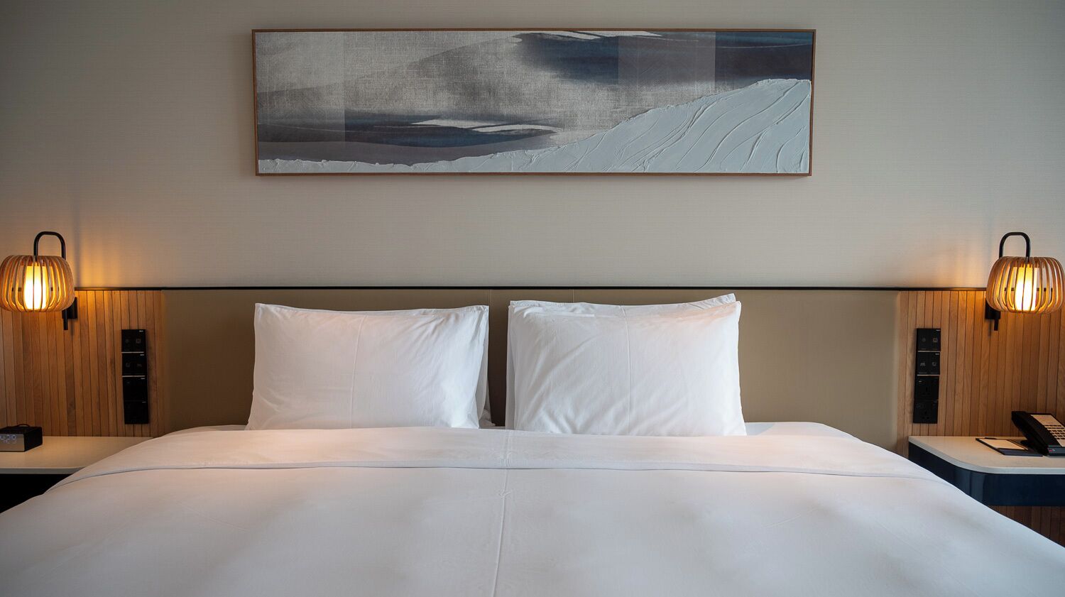 Habitación de hotel con una cama grande, dos lámparas de noche, un cuadro sobre la cama y un panel de pared de madera.