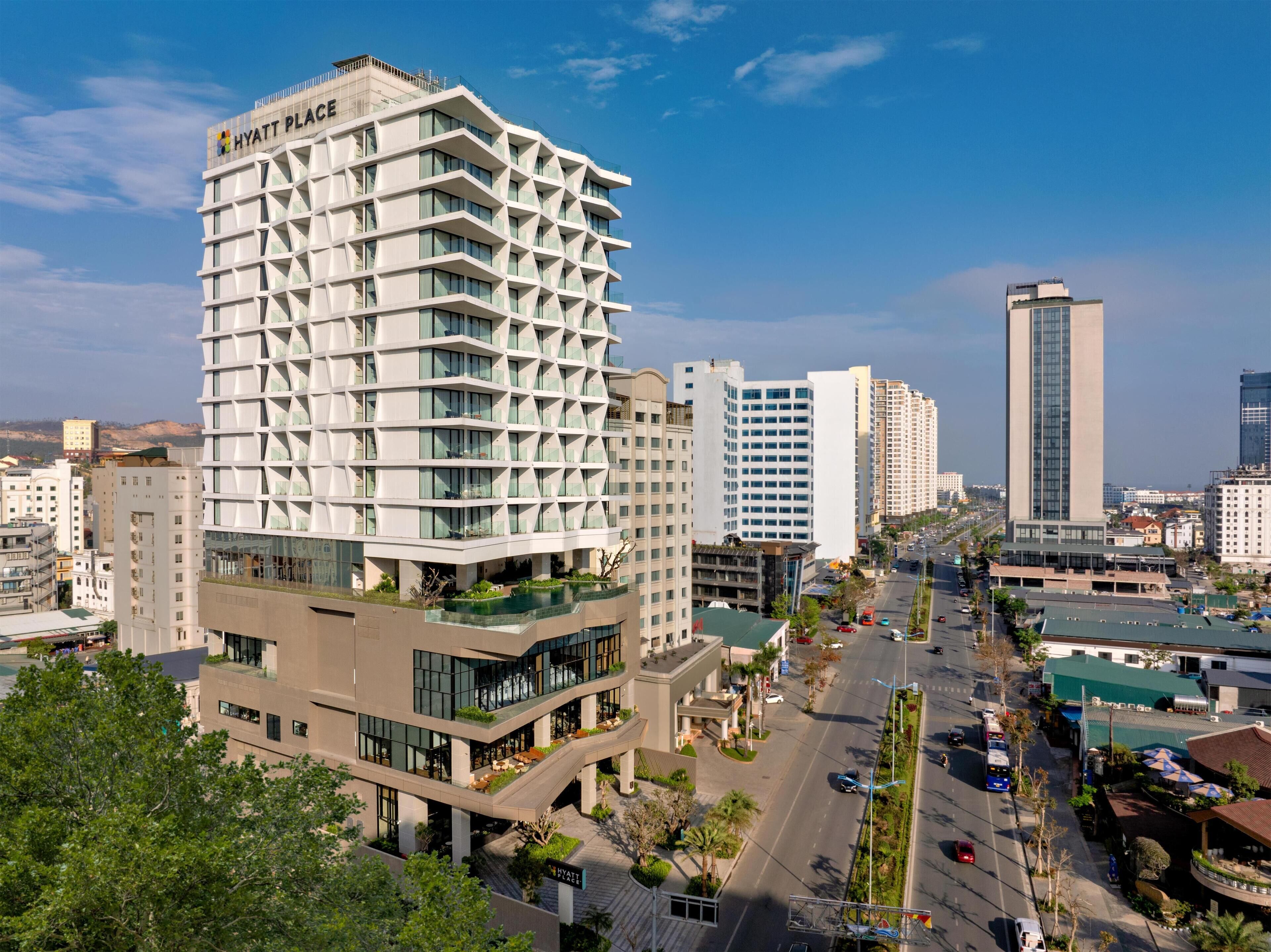 A modern Hyatt Place hotel with a unique geometric facade, multiple balconies, and a rooftop garden.