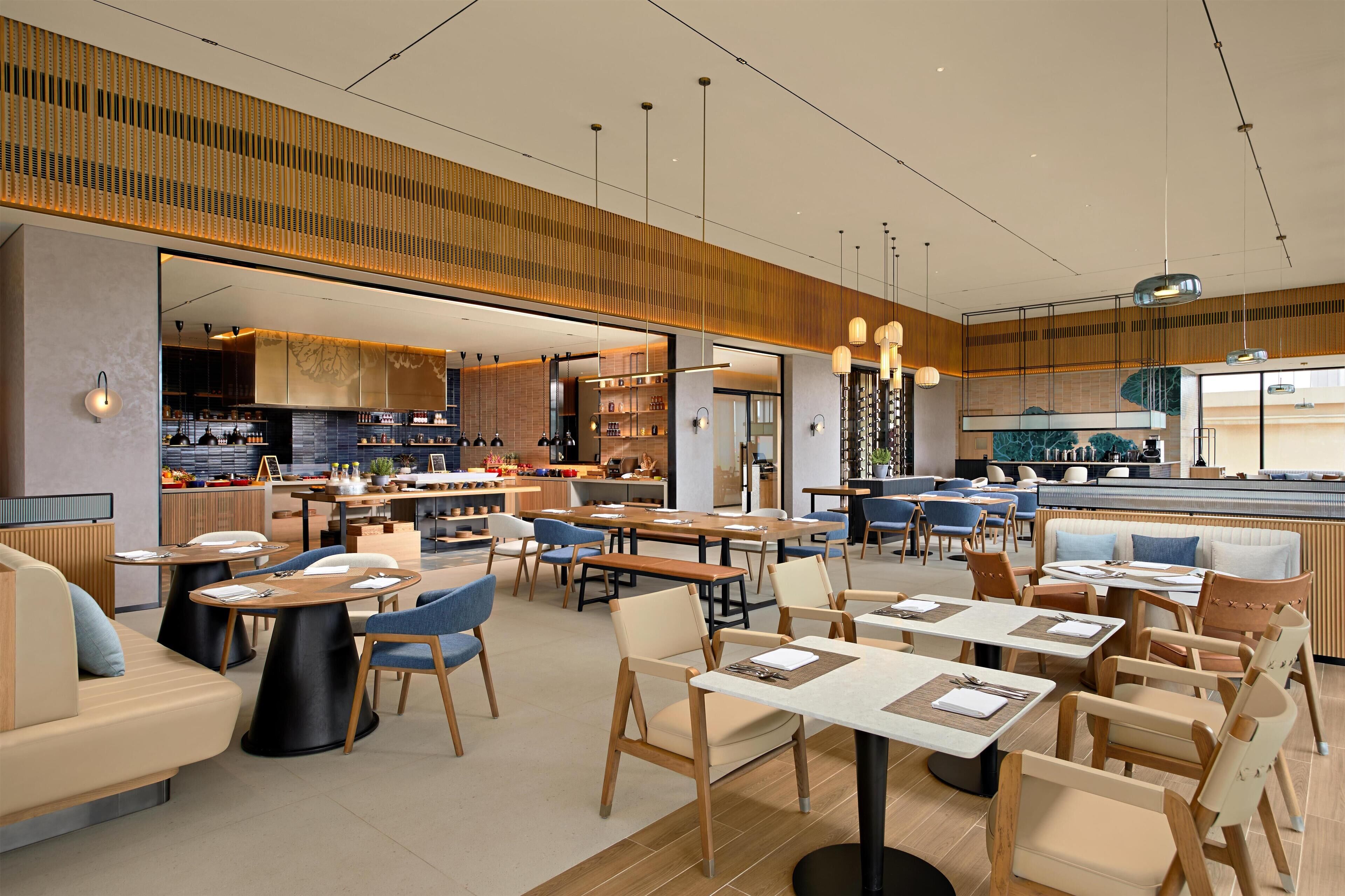A modern restaurant with a variety of seating options including tables and booths, a visible kitchen area, and a bar.