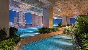 Un espace piscine intérieur moderne, avec une eau d’un bleu limpide, entouré de verdure et offrant une vue sur le paysage urbain la nuit.