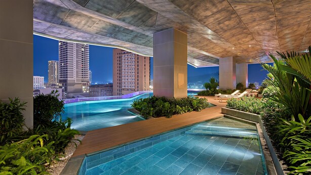 Un espace piscine intérieur moderne, avec une eau d’un bleu limpide, entouré de verdure et offrant une vue sur le paysage urbain la nuit.
