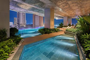 A modern indoor pool area with clear blue water, surrounded by greenery and a cityscape view at night. - Hyatt Place Ha Long Bay, Bai Chay (Bai Chay)