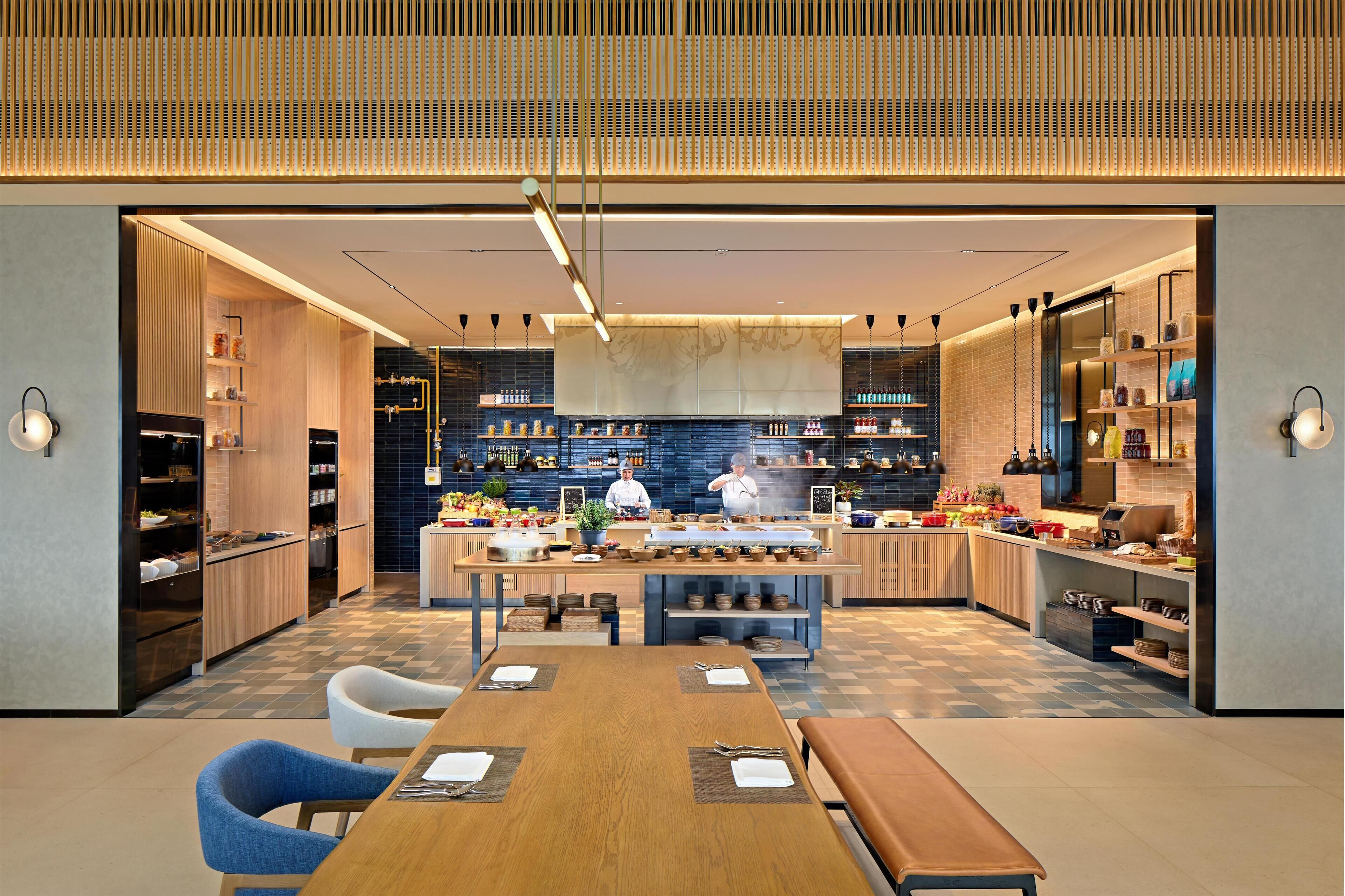 A modern restaurant with a central island, wooden cabinetry, and a chef preparing food.