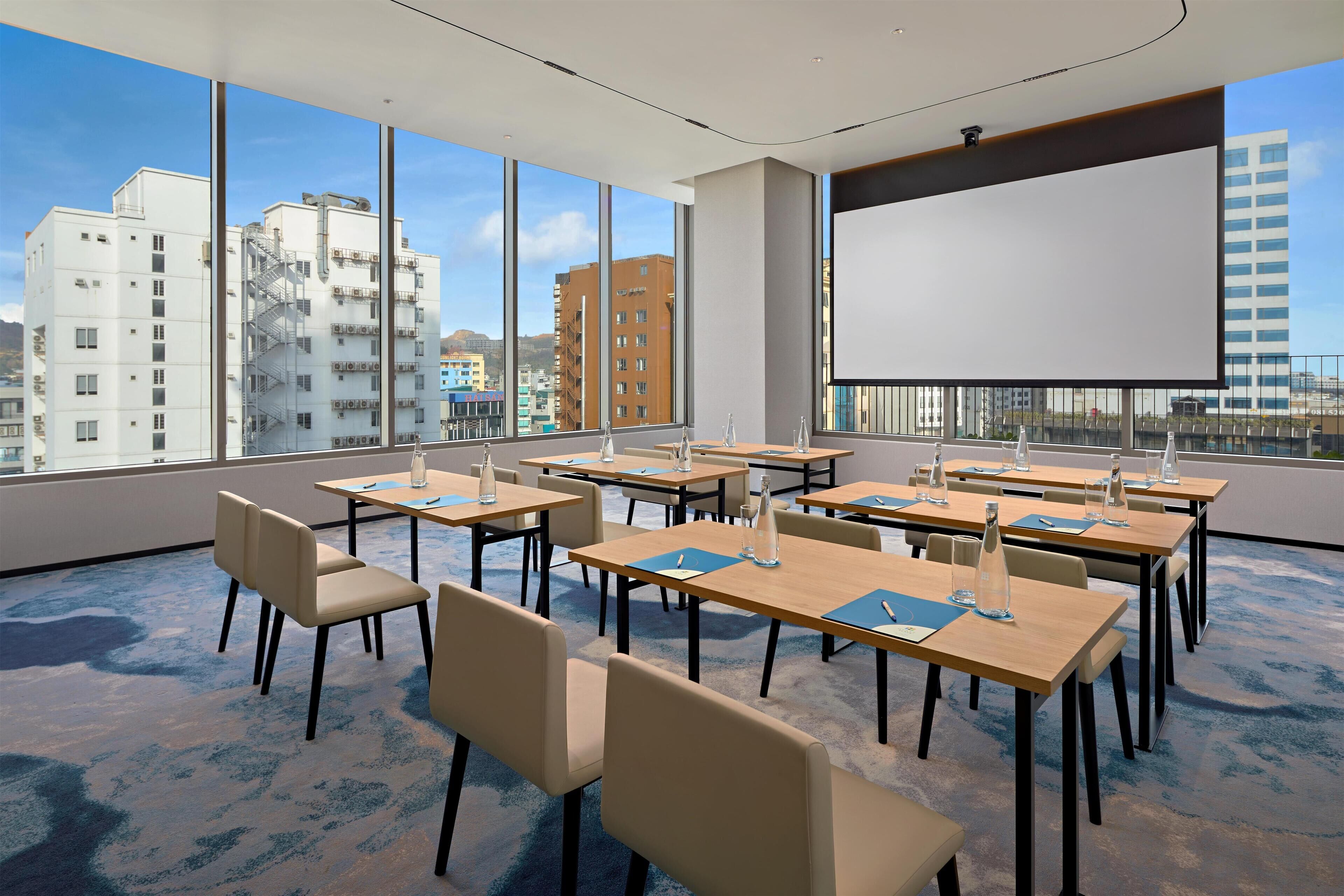 A conference room with large windows, multiple tables, and chairs, equipped with water bottles and notepads.