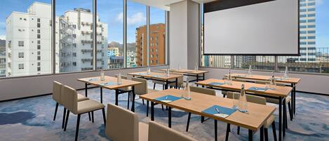 Un salón de conferencias con amplios ventanales, varias mesas y sillas, equipado con botellas de agua y blocs de notas.
