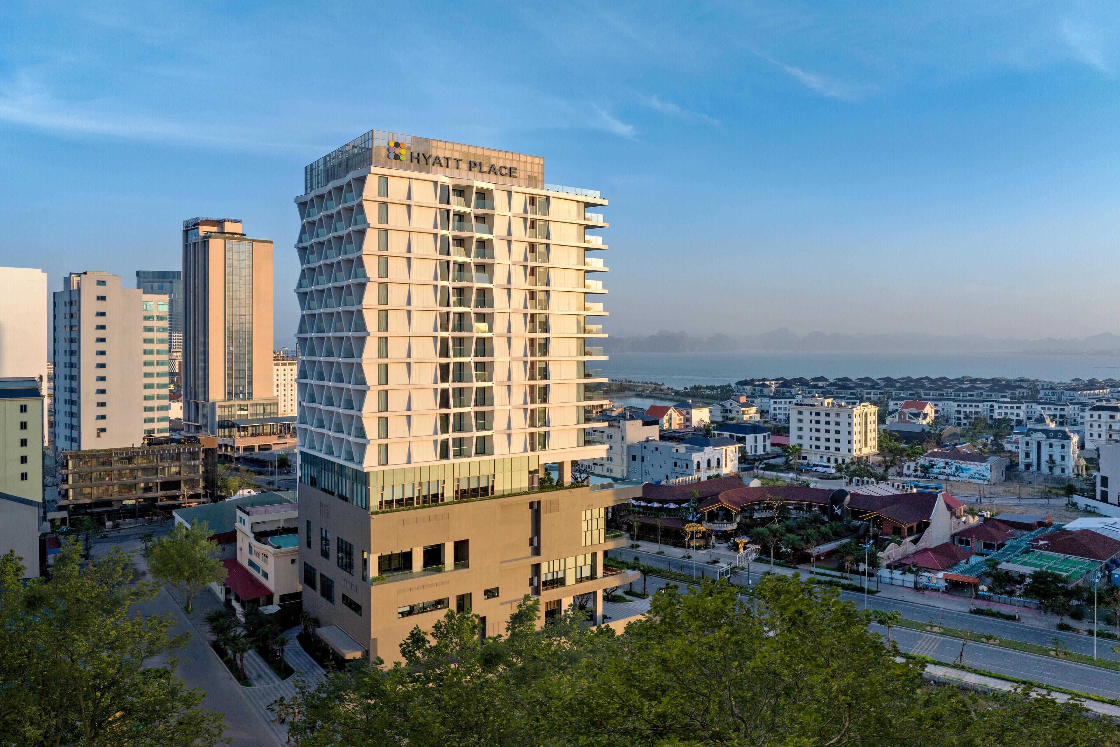 A modern hotel with a unique geometric facade, located in a cityscape with a view of the sea.