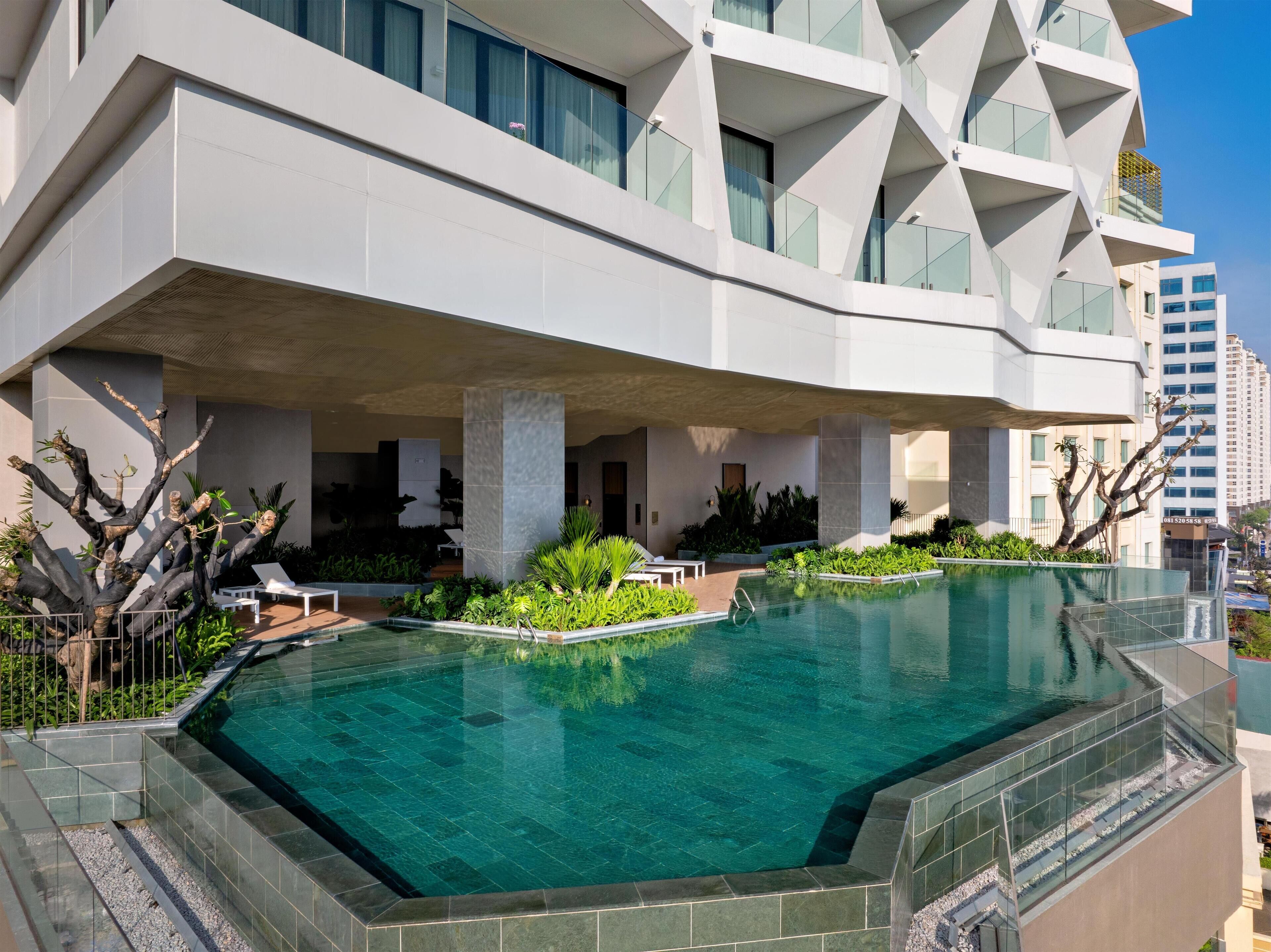 A modern hotel with a large outdoor pool, covered seating areas, and a unique architectural design.