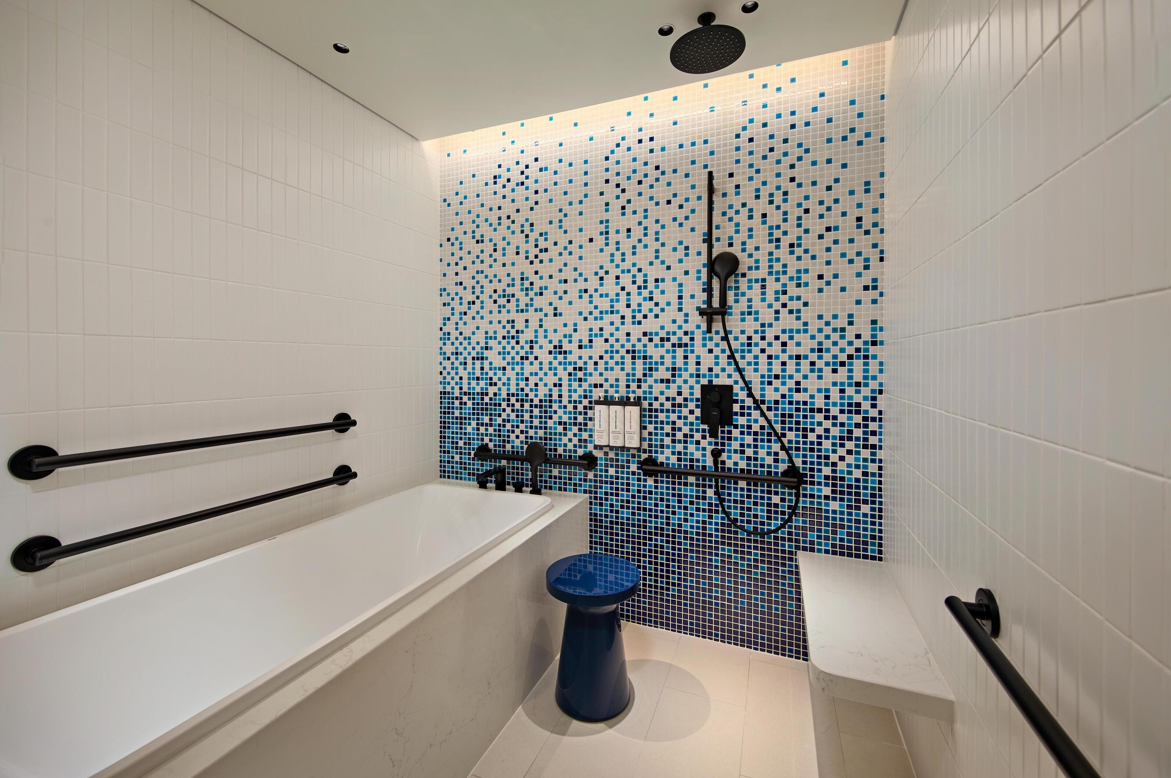 Een moderne badkamer met een witte badkuip, een blauw toilet en een douchegedeelte met een mozaïektegelwand.