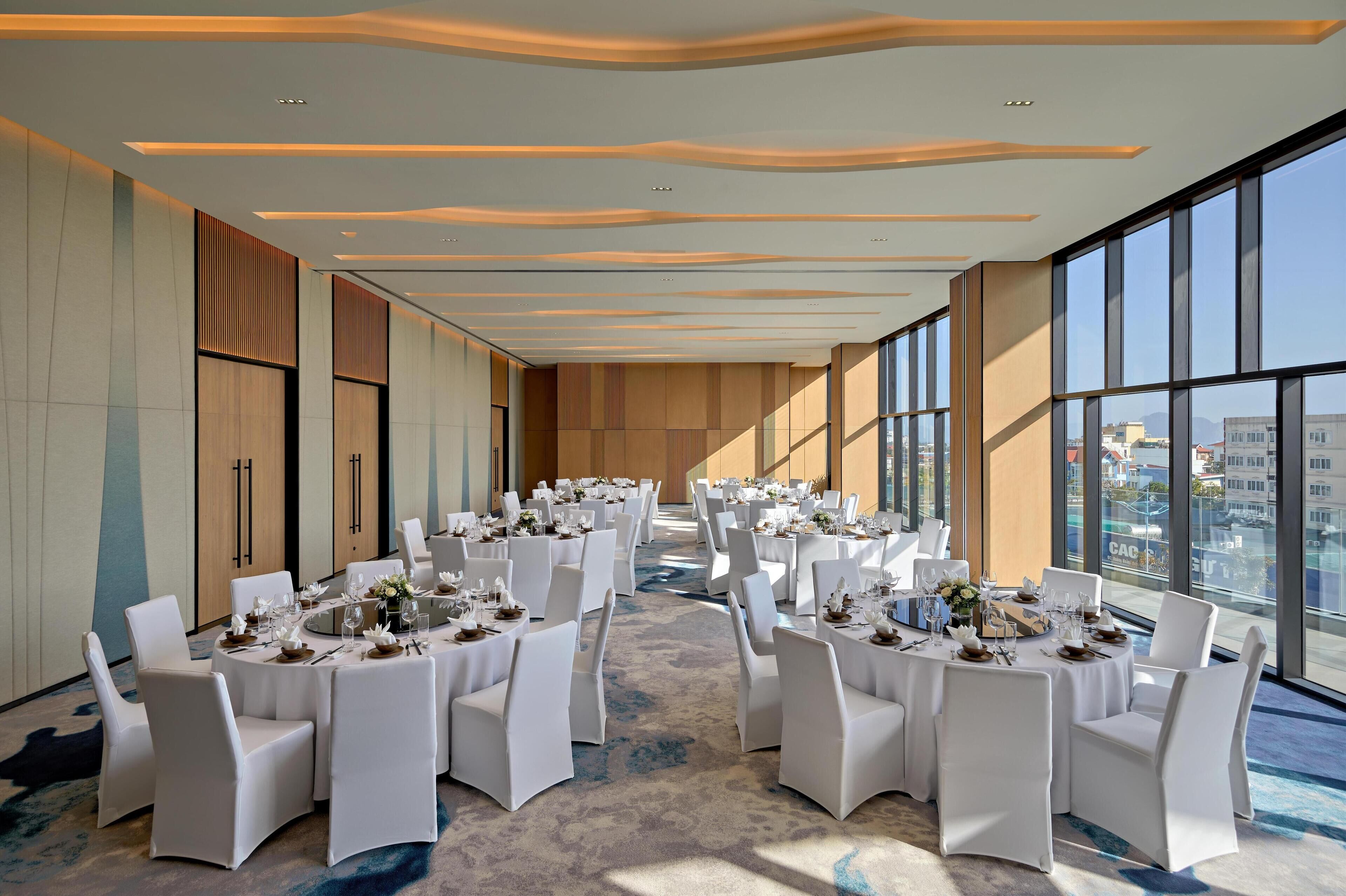 A conference room with round tables, white chairs, and a carpeted floor.