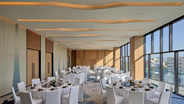 Une salle de conférence avec des tables rondes, des chaises blanches et un sol recouvert de moquette.