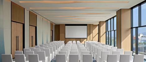 A conference room with rows of white chairs, a large screen, and a modern ceiling design.
