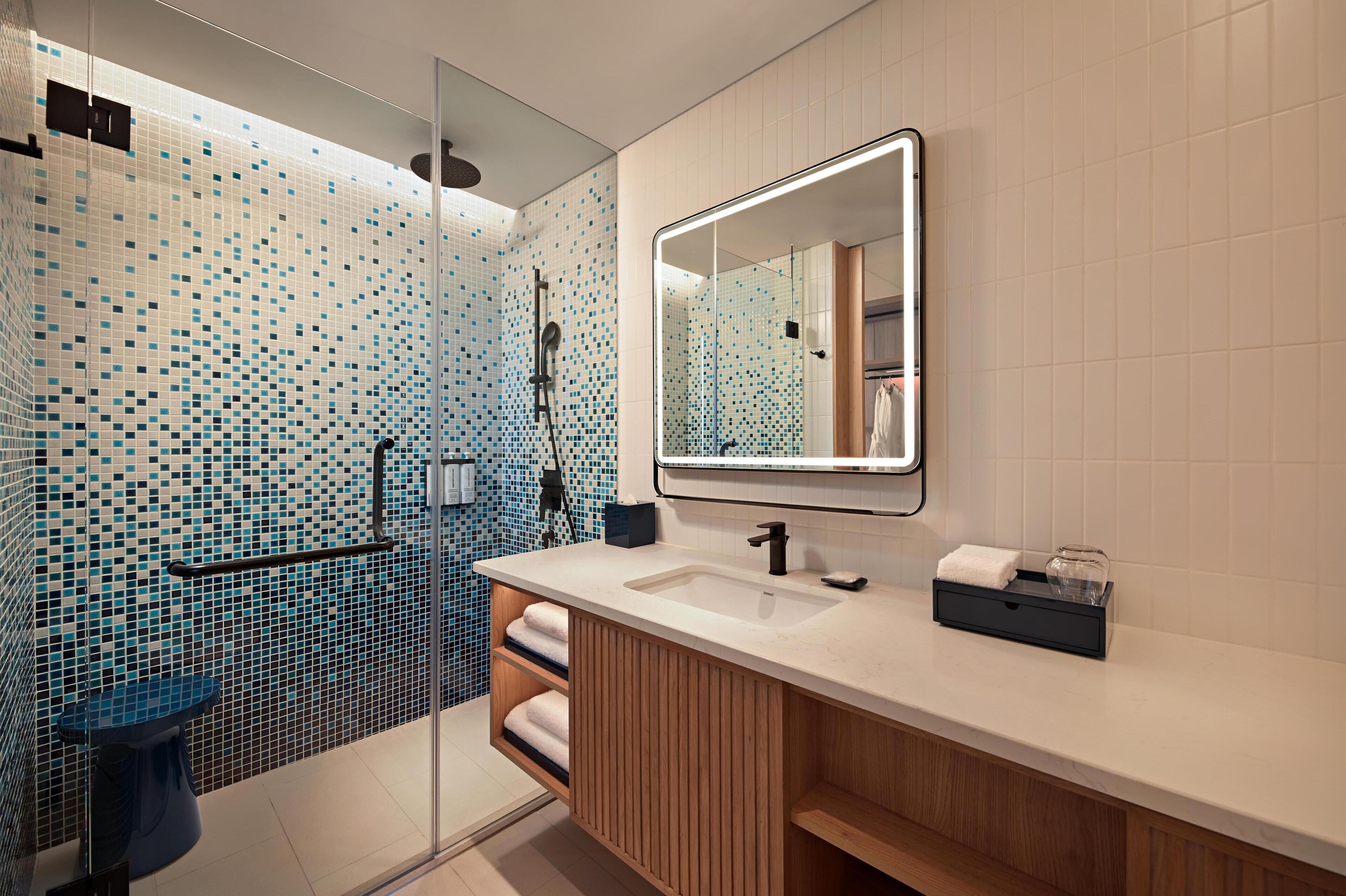 Un baño moderno con cabina de ducha de vidrio, un espejo grande y un tocador de madera.