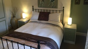 A bedroom with a bed, two bedside tables, a nightstand, a vase with branches, and a painting of two kangaroos on the wall.