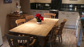 A wooden dining table with six chairs, a potted plant, and a kitchen in the background.