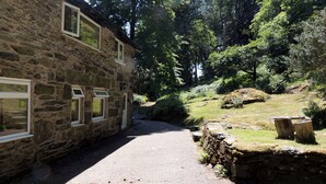 Un bâtiment en pierre doté de nombreuses fenêtres, un chemin pavé et un paysage naturel avec des arbres et une zone herbeuse.