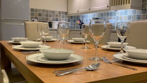 Une cuisine moderne avec une table à manger en bois, mise pour quatre personnes, et agrémentée d’assiettes, de bols et de verres à vin blancs.