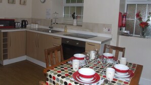 A kitchen with a dining area, equipped with a microwave, toaster, sink, and a dining table set with plates, bowls, and glasses. - Sygun Cottage 40 mins walk to Watkin Waterfalls, Snowdon (Beddgelert)