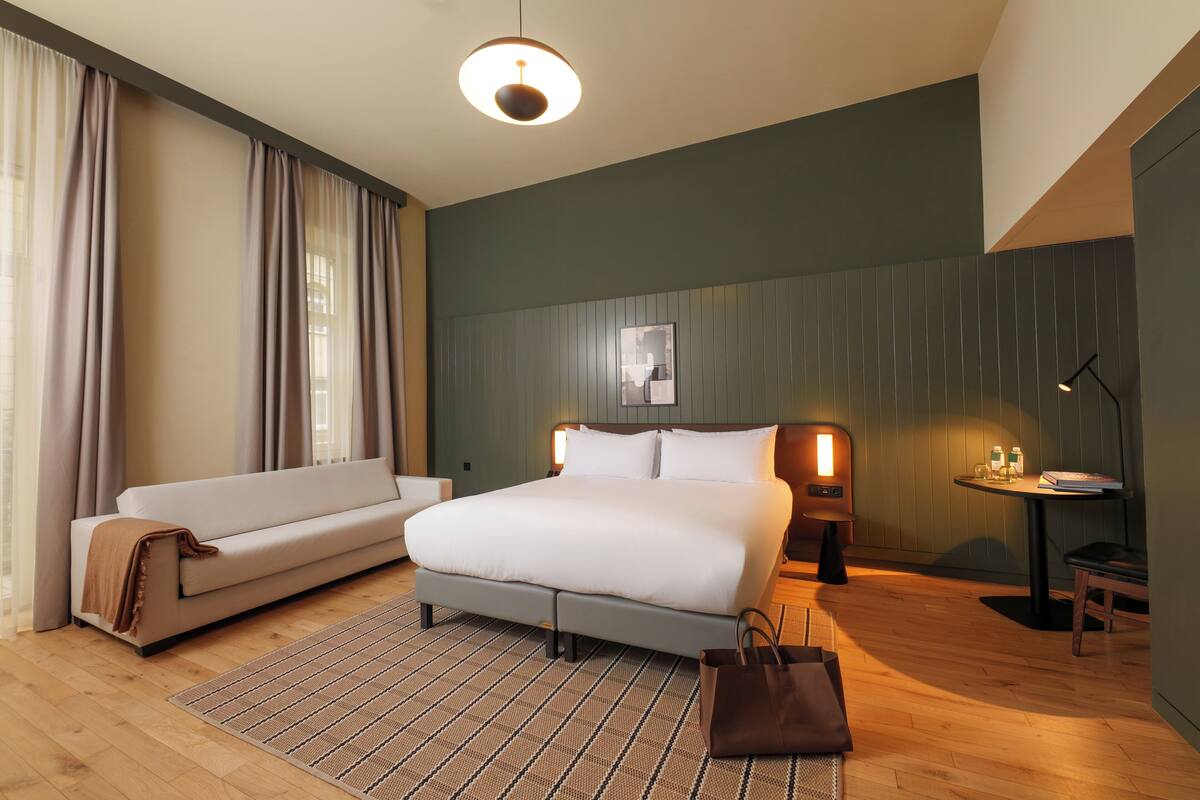 A modern hotel room with a bed, a sofa, a small table, and a lamp.