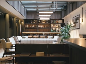 Un área de bar moderna con asientos, techo alto con vigas a la vista y varias botellas en estantes.