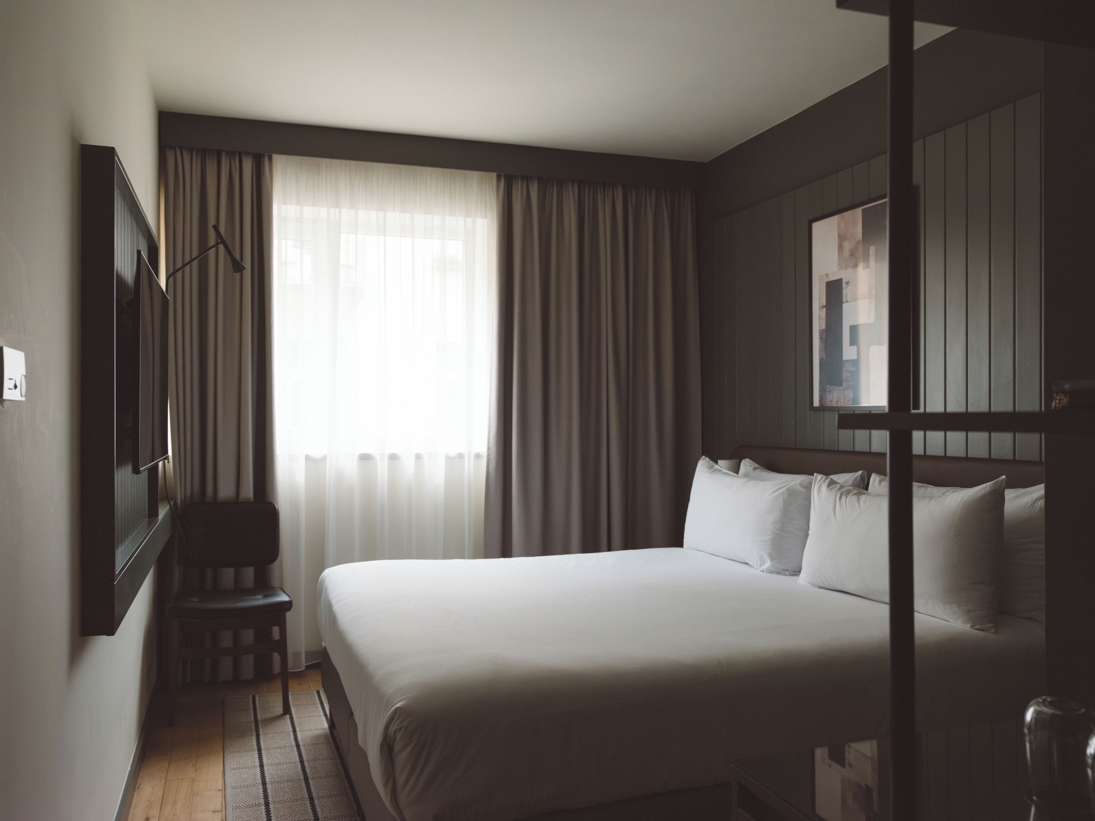 A hotel room with a large bed, a chair, a TV, and a window with curtains.