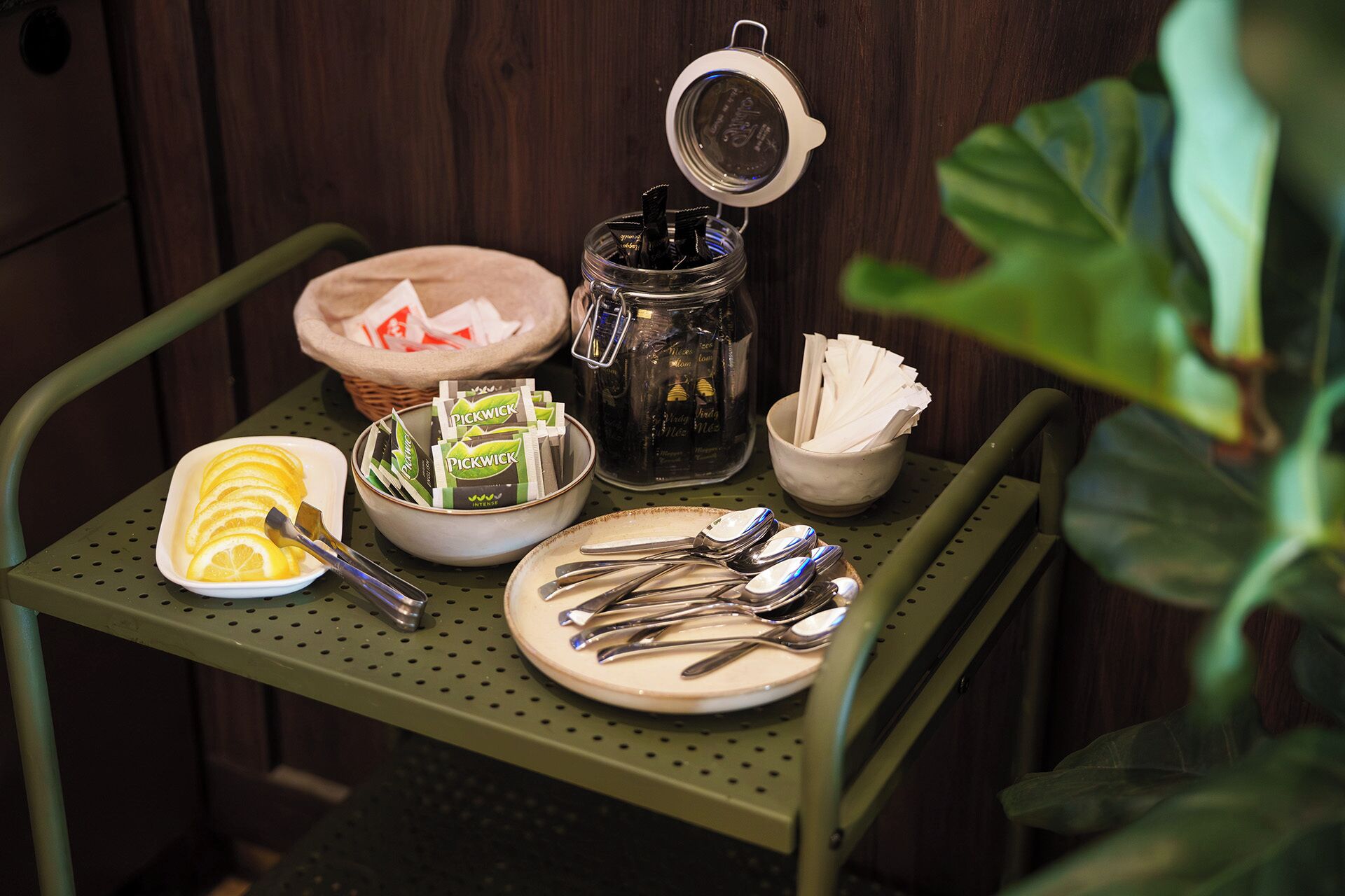 A metal table with a glass jar, a bowl of lemons, a bowl of napkins, and a plate with cutlery.