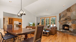 A spacious living area with a stone fireplace, a dining table with chairs, and a kitchen in the background.