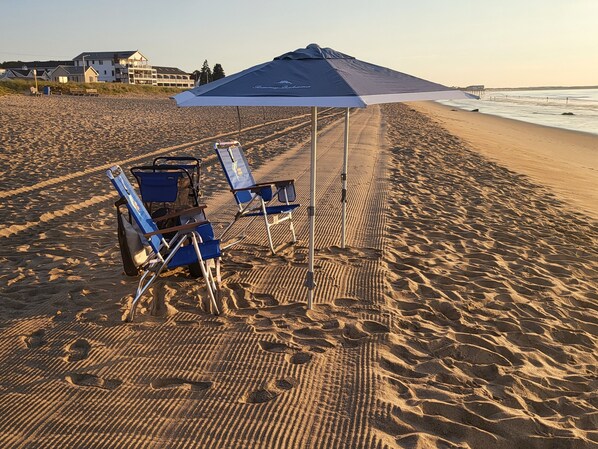 A beach with two blue lounge chairs and an umbrella under a building.