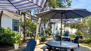 An outdoor patio with picnic tables and chairs, surrounded by trees and a house.