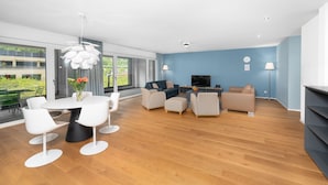 A modern living room with a round dining table, white chairs, a sofa set, and a TV.