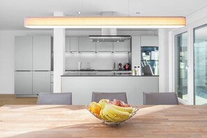 A modern kitchen with white cabinets, a central island, and a fruit bowl on the dining table.