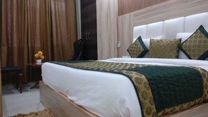 Une chambre d’hôtel avec un grand lit, une tête de lit en bois, une petite table de chevet ornée d’un vase de fleurs et une armoire de couleur sombre.