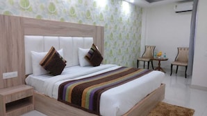 Une chambre d’hôtel avec un grand lit, une tête de lit en bois, deux chaises, une petite table et un papier peint à motifs.