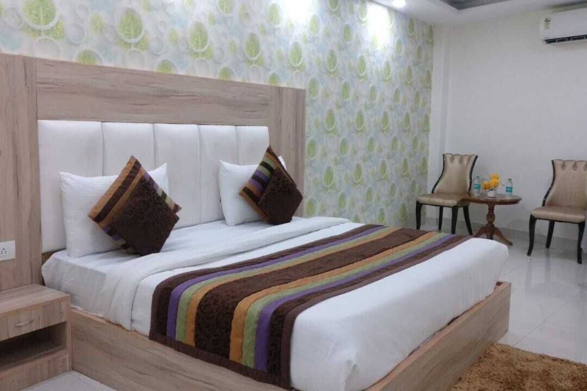 A hotel room with a large bed, a wooden nightstand, a small table with chairs, and a patterned wallpaper.