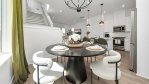 A modern dining area with a round table, white upholstered chairs, a black pedestal base, and a chandelier.