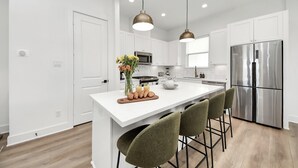 A modern kitchen with white cabinetry, a stainless steel refrigerator, and a central island with bar stools.