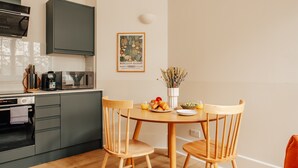 Et moderne køkken med lysegrå skabe, en mikrobølgeovn og en kaffemaskine. Der er et indrammet billede på væggen og et bord med stole.