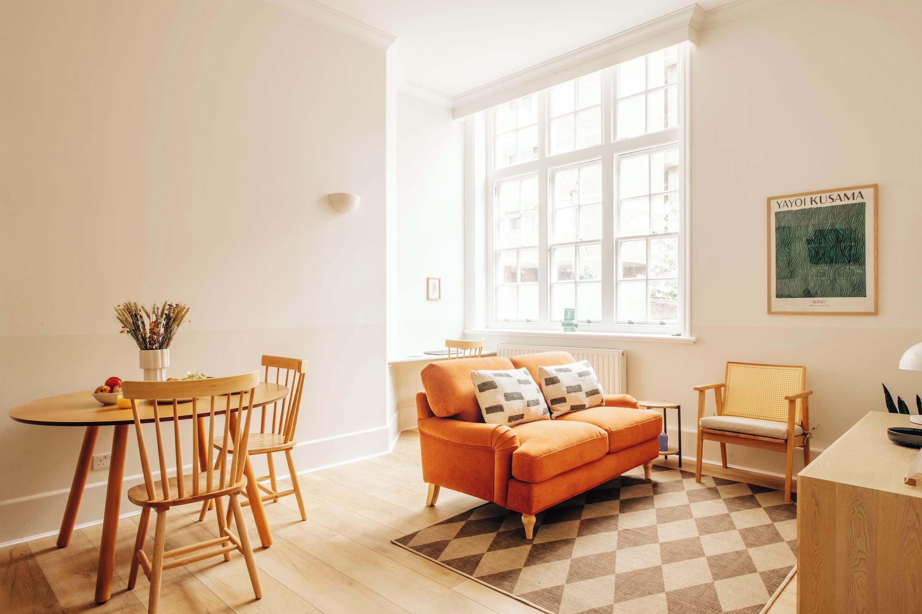 Ein helles Zimmer mit großem Fenster, einem Holzespeisetisch mit Stühlen, einer Couch und einem kleinen Beistelltisch.