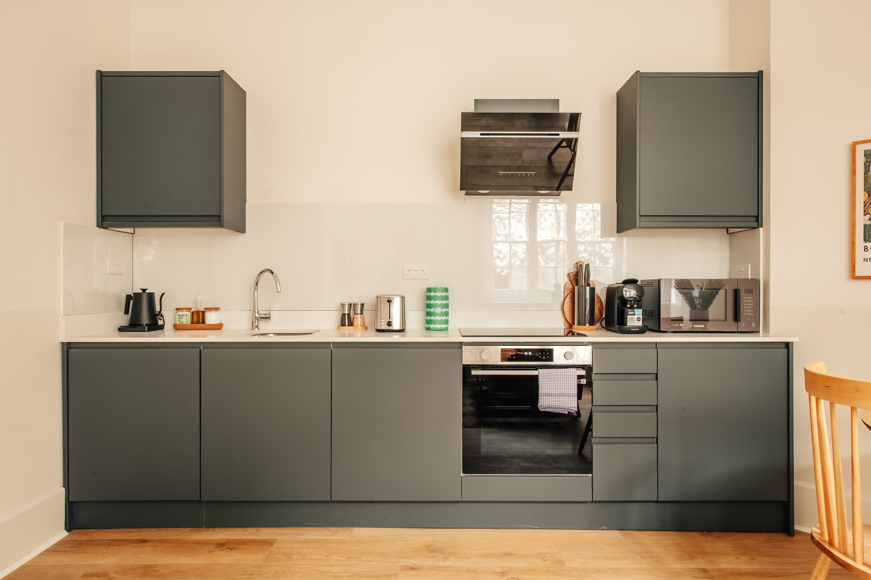 Une cuisine moderne avec des meubles gris, une hotte en acier inoxydable, un four à micro-ondes et un four encastré.
