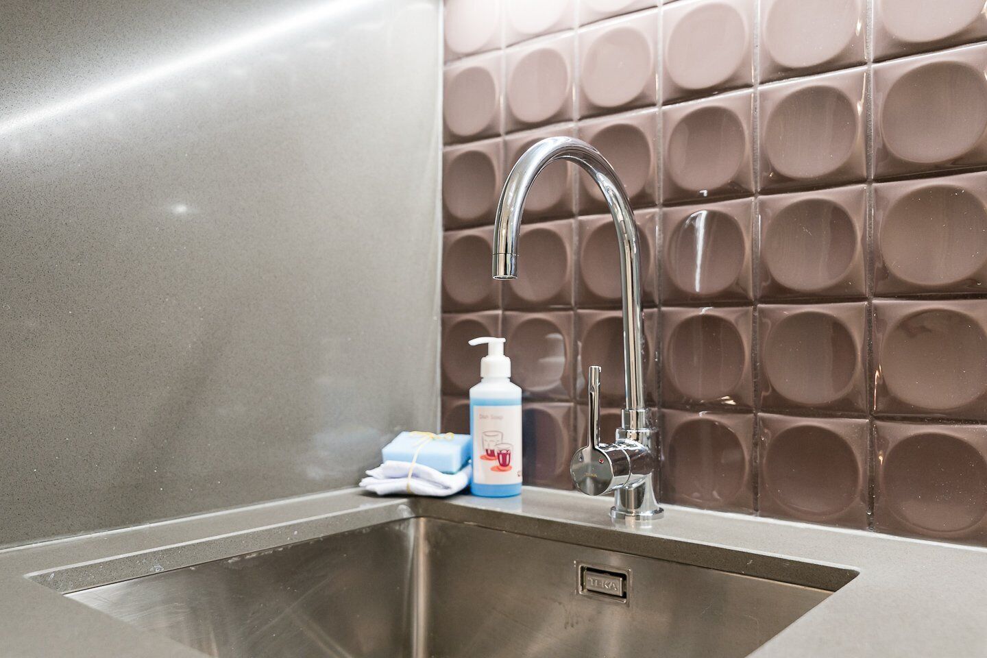 A modern bathroom with a stainless steel sink, a chrome faucet, and a soap dispenser.