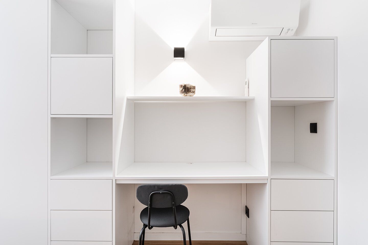 Une pièce au décor minimaliste, avec des étagères blanches, un bureau et une chaise.